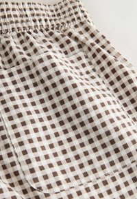 Gros plan sur la ceinture élastique et la poche en tissu à carreaux marron et blanc sur le vêtement.