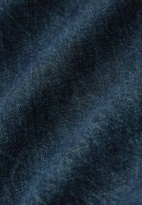 Tamno plavi denimski materijal s teksturiranom površinom, koji prikazuje suptilne varijacije u boji i uzorku tkanja, ističući meku, izdržljivu kvalitetu.