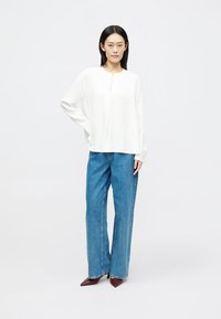 Weiße Bluse mit langen Ärmeln und Teilknopfleiste, kombiniert mit hoch taillierten Jeans aus Denim im weit geschnittenen Stil und in heller Waschung.