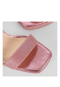 Sandali con tacco a blocco rosa con una fascia luccicante e una superficie superiore brillante, caratterizzati da un design a punta quadrata e dettagli testurizzati sulla fascia.