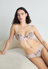 Spitzen-BH und Höschen-Set in Hellrosa mit floraler Stickerei. Der BH hat verstellbare Träger und gewellte Kanten; der Stoff scheint durchsichtig zu sein.
