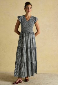 Maxikleid im schwarz-weißen Karomuster, mit V-Ausschnitt, Rüschensäumen und gestuftem Rock. Kombiniert mit bordeauxfarbenen Mary Jane Schuhen.