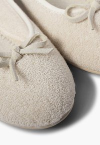 Ballerine beige in tessuto testurizzato con superficie morbida, caratterizzate da un piccolo fiocco in camoscio sulla parte anteriore. Punta rotonda e suola flessibile.