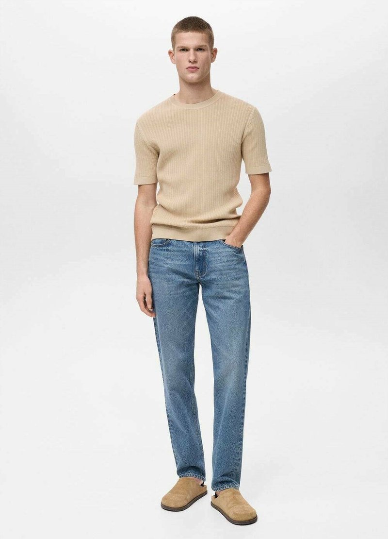 Beige žebrovaný svetr s krátkým rukávem, světle modré džíny rovného střihu a hnědé slip-on boty. Oblečení má pohodlný střih a jednoduchý design.
