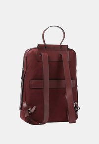 Mochila marrón con correas dobles para los hombros, un asa superior, cremallera lateral y un panel trasero plano. Fabricada con un tejido duradero y acentos de cuero suave.