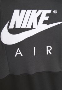 Nike Air logo in white embroidery on dark grey and black fabric background.