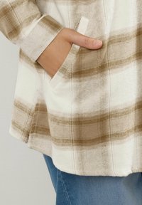 Beige ja kreemikas flanellpaita, pehmea tekstuuriga, küljetasku ja v-kaelusega, koos siniste teksadega.