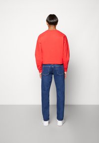 Sudadera roja de algodón combinada con jeans de mezclilla azul. Los jeans tienen un corte recto y bolsillos traseros. Estilizados con zapatillas blancas.