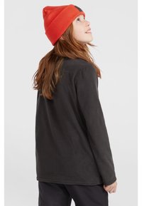 Felpa nera in pile con maniche lunghe, caratterizzata da una texture morbida e un fit rilassato. Sulla testa è indossato un berretto lavorato a maglia arancione.