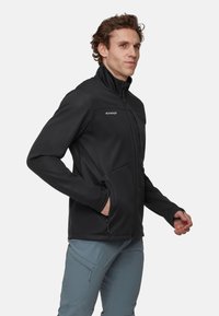 Schwarze Softshell-Jacke mit hohem Kragen, Reißverschluss-Taschen und flexiblem Material. Das Design zeigt eine minimalistische Ästhetik.