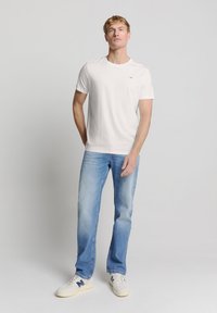 Witte katoenen t-shirt met korte mouwen, ronde hals; gecombineerd met lichtblauwe rechte jeans en witte sneakers met blauwe accenten.
