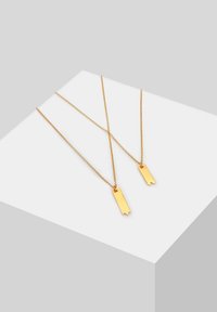 Goldfarbene Halsketten mit zwei Anhänger-Tags. Die Ketten haben feine Glieder, und die Tags sind rechteckig mit Aussparungen an den unteren Kanten.