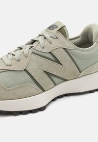 Light green athletic shoes featuring suede and mesh materials, a prominent "N" logo, and a textured sole for grip.