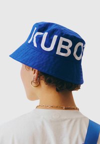 Niebieska czapka typu bucket wykonana z teksturowanej tkaniny z wyraźnym białym napisem. Posiada szerszy daszek i lekko luźną koronę.