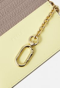 Læderaccessory med en glat gul overflade og tekstureret taupe topsektion. Inkluderer en gylden kæde og beslag. Brandlogo prægede.