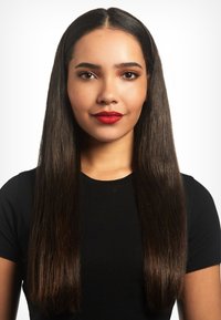 Jonge vrouw met lang steil donker haar, met rode lippenstift en een zwart shirt, recht vooruitkijkend op een witte achtergrond.