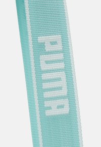 Vaaleansininen kudottu hihna valkoisella "PUMA"-logotekstillä, jossa on teksturoitu pinta ja litteä muotoilu.