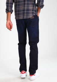 Mörkblå denimjeans med rak passform, utrustade med ett lädermärke på baksidan och en slät yta. Används med vita sneakers.