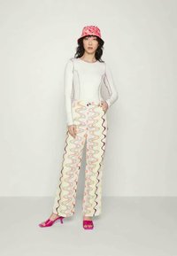 Top branco de mangas compridas com detalhes de costura, combinado com calças largas padrão zigzag coloridas e sandálias de salto alto cor-de-rosa. Chapéu balde vermelho.