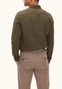 Olijfgroene lange mouwen shirt met een rechte kraag, knoopmanschetten en zichtbare stiksels, gedragen met kaki-kleurige broek met achterzakken.