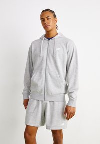 Grå zip-up hættetrøje med snoretræk, der har forlommer og ribbede ærmer, parret med matchende shorts. New Balance-logo på begge dele.