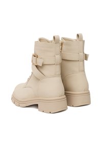 Beżowe botki za kostkę z teksturowanego materiału, z okrągłym noskiem, bocznym zamkiem błyskawicznym oraz owijającym paskiem z dodatkiem złotej klamry. Masywna podeszwa.