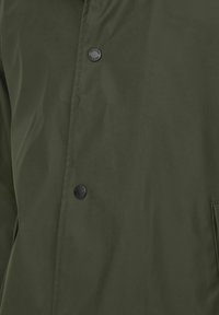 Jachetă olive din material neted, rezistent la apă, cu închidere prin buton și buzunar lateral, având un design elegant și minimalist.