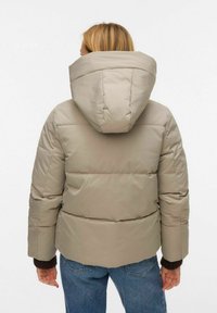 Doudoune beige avec une grande capuche, un design matelassé et des poignets côtelés. Le matériau semble lisse et légèrement réfléchissant. Vue de dos montrée.