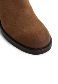 Stivale alla caviglia in suede marrone con punta arrotondata, caratterizzato da una suola in gomma nera e dettagli cuciti lungo il bordo.