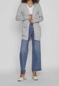 Grå cardigan med v-ringning, ribbade ärmslut och två framfickor, tillsammans med högmidjade, blå vida jeans och krämfärgade klackskor.