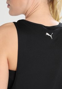 Svart atletisk linne med texturerad tyg, ärmlös design och en liten vit Puma-logotyp vid nacköppningen.