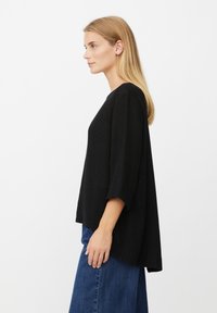 Schwarzer Pullover mit lockerem Schnitt, Bootsausschnitt und dreiviertellangen Ärmeln, aus strukturiertem Stoff, kombiniert mit Jeans im weiten Bein.