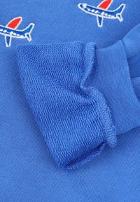 Camicia blu con orlo delle maniche strutturato, caratterizzata da grafiche di aerei ricamate in bianco e rosso sul tessuto. Realizzata in morbido cotone.