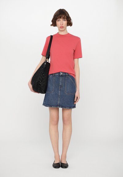 Red cotton t-shirt paired with a blue denim skirt features patch pockets. Model carries a black textured handbag and wears black flats.