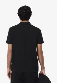 Mustapaitainen lyhythihainen polo-paita, joka on valmistettu pehmeästä kankaasta. Paitassa on kaulus, suora helma ja minimaalinen ompelu yksityiskohtia. Yhdistetty tummiin housuihin.