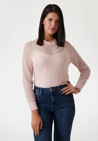Lichtroze trui met een ronde hals, een textuurpaneel op de borst en lange mouwen. Gecombineerd met hooggewaist donkerblauwe jeans.