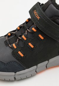 Sneaker neri e grigi con accenti arancioni. Presenta un colletto imbottito, una fascia in velcro e una suola in gomma testurizzata. Sistema di allacciatura distintivo.