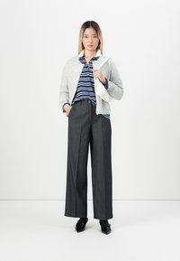 Siv kardigan preko mornarsko modre in bele proste polo majice, v kombinaciji z visokim pasom temno sivimi širokimi hlačami in črnimi čevlji.