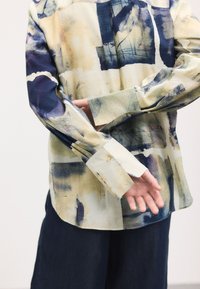 Button-up shirt featuring an abstract watercolor pattern in yellow, navy, and blue. Long sleeves with single cuffs, made from lightweight fabric.