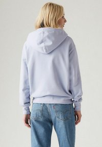 Felpa lavanda con un grande cappuccio, maniche lunghe e orlo a costine. Abbinata a jeans azzurri a vita alta con tasche.