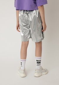 Shorts argento, lucidi, fino al ginocchio, con vita elastica, abbinati a calze bianche con testo viola e nero e sneakers bianche.
