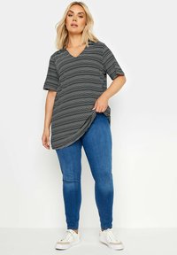 T-shirt a rayas en blanco y negro con escote en V y mangas cortas, combinado con jeans ajustados azules y zapatillas blancas, presentado en un modelo.