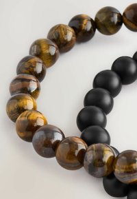 Zwei Perlenarmbänder: eines mit polierten Tigeraugensteinen in braunen und schwarzen Farbtönen, das andere mit matten schwarzen Perlen, die im Textur und Glanz kontrastieren.