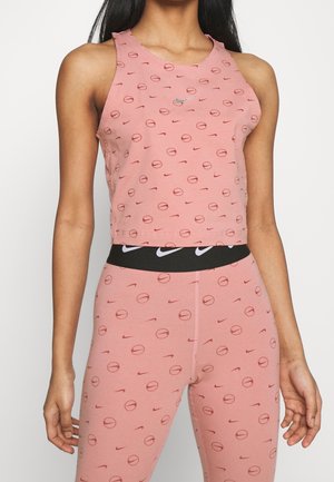 Kobieta w różowym sportowym crop topie i legginsach z małymi wzorami piłki do koszykówki i logo Nike Swoosh, czarny pas z białymi logo Swoosh.