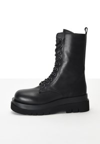 Černá kožená bojová bota s kulatou špičkou, silnou podrážkou, šněrovacím předním dílem, stříbrnými očky a poutkem na vrchu.