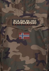 Kamuflage pullover jakke i nuancer af brun og grøn. Har et stort logo patch og en brodering af Norges flag. Inkluderer en lynlås-lomme.