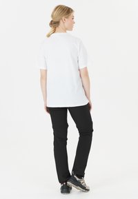 T-shirt blanc à manches courtes avec un col arrondi, associé à un pantalon de plein air noir. Le mod�èle montre une vue de profil, les chaussures présentent une semelle robuste.