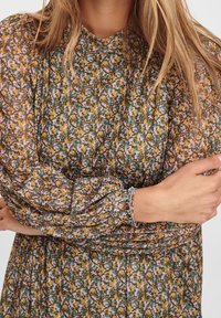 Long-sleeve, floral-patterned dress featuring shades of green, yellow, and pink. Semi-sheer fabric with gathered sleeves, textured surface.