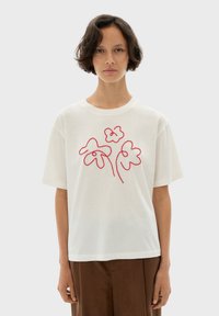 Vit t-shirt med korta ärmar och röd blommig brodyr. Lös passform med rund halsringning, tillverkad av mjukt bomullsmaterial.