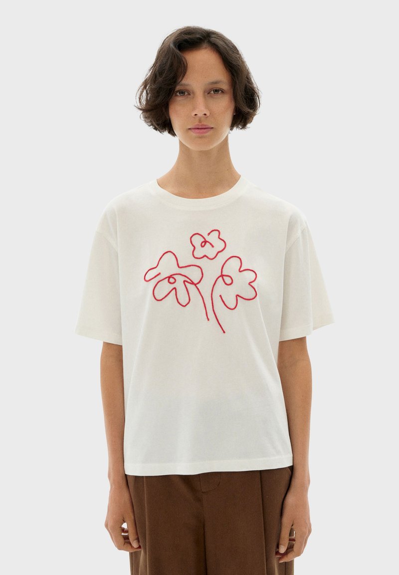 Vit t-shirt med korta ärmar och röd blommig brodyr. Lös passform med rund halsringning, tillverkad av mjukt bomullsmaterial.